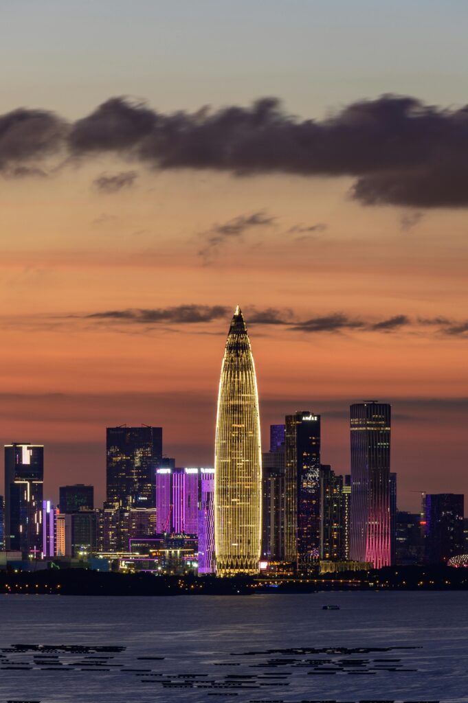 pexels photo 12668188 12668188 Illuminated city skyline featuring a distinct tall building at sunset.